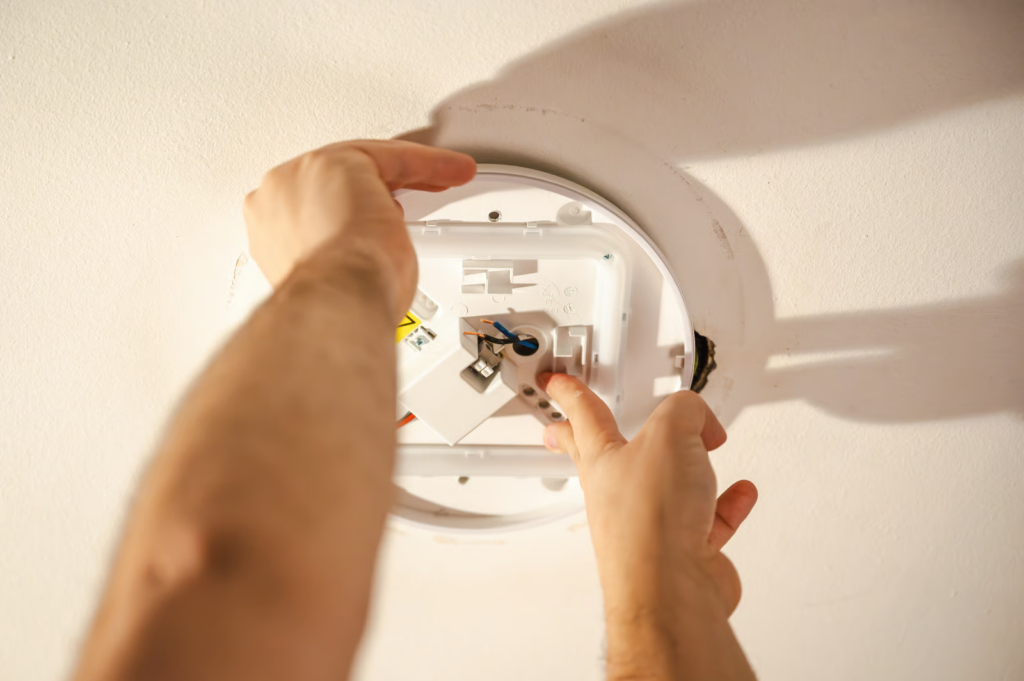 Technician completing smoke detector base replacement on a ceiling-mounted fire alarm device.