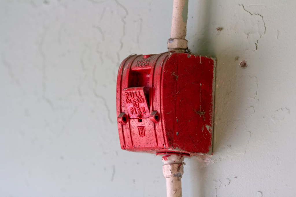 Weathered vintage fire alarm pull station on wall representing early fire alarm technology history