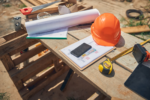Construction site blueprint and hard hat on wooden pallet representing FPPM requirements and fire prevention planning on a jobsite